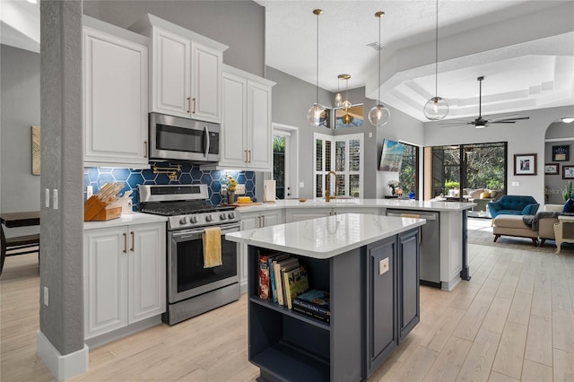 kitchen featuring kitchen peninsula, stainless steel appliances, a raised ceiling, ceiling fan, and white cabinetry