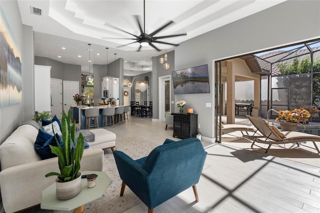 living room with ceiling fan, a towering ceiling, and light wood-type flooring