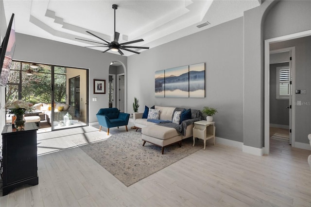 living room with a raised ceiling, ceiling fan, and light hardwood / wood-style flooring