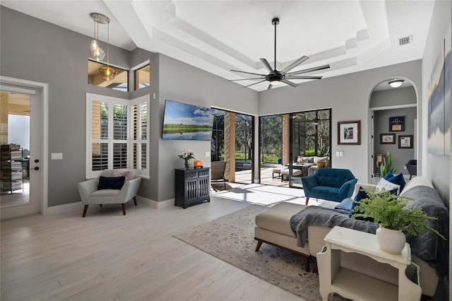 living room featuring a raised ceiling, ceiling fan, and light wood-type flooring