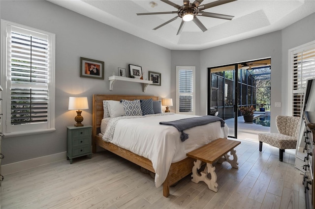 bedroom featuring access to outside, a raised ceiling, ceiling fan, and light hardwood / wood-style flooring