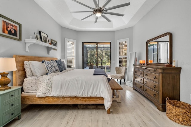 bedroom with ceiling fan, light wood-type flooring, and a tray ceiling