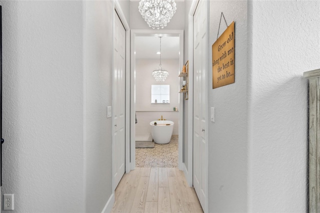 hallway with tile walls, light hardwood / wood-style flooring, and an inviting chandelier