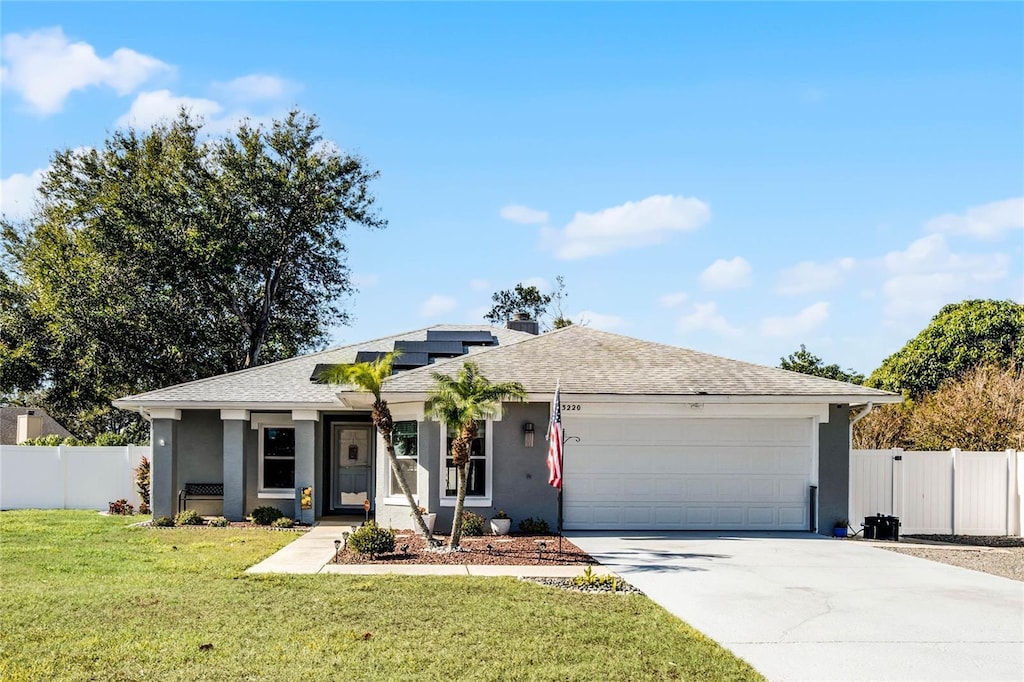 single story home with solar panels, a garage, and a front lawn