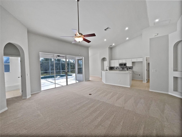 unfurnished living room with ceiling fan, light colored carpet, and a towering ceiling