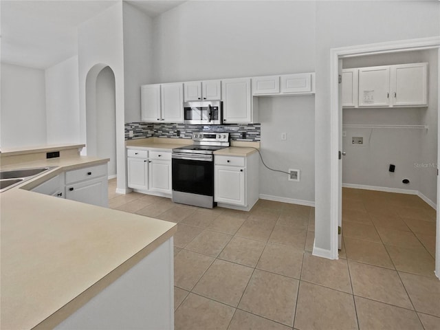 kitchen with backsplash, stainless steel appliances, sink, light tile patterned floors, and white cabinetry