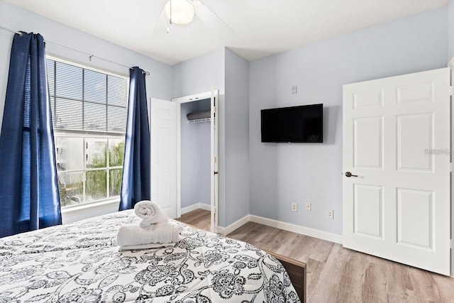 bedroom with multiple windows, a wall mounted air conditioner, light hardwood / wood-style flooring, and ceiling fan