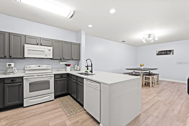 kitchen with sink, white appliances, light hardwood / wood-style floors, and kitchen peninsula