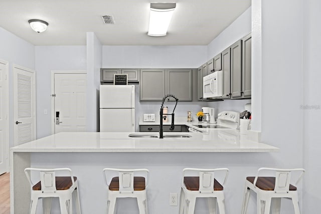 kitchen featuring a breakfast bar, sink, white appliances, and kitchen peninsula