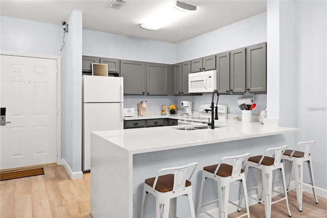 kitchen featuring sink, a breakfast bar area, gray cabinets, kitchen peninsula, and white appliances