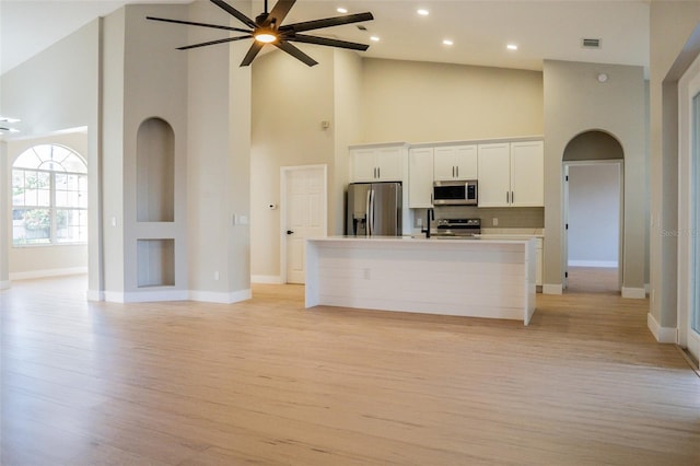 kitchen featuring stainless steel appliances, ceiling fan, a center island with sink, a high ceiling, and white cabinetry