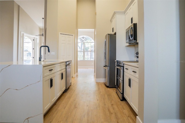 kitchen with sink, stainless steel appliances, vaulted ceiling, white cabinets, and light wood-type flooring