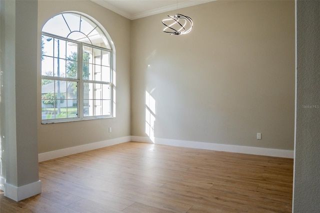 empty room featuring light hardwood / wood-style flooring, crown molding, and a notable chandelier