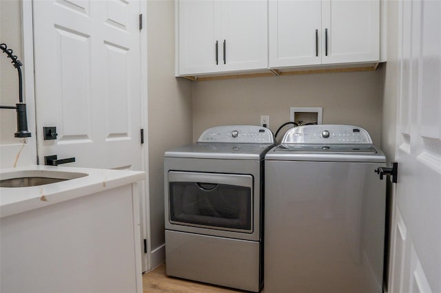 clothes washing area with washing machine and clothes dryer, cabinets, and light hardwood / wood-style floors