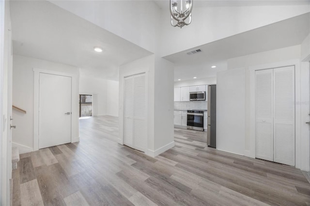 unfurnished living room with a towering ceiling, a chandelier, and light hardwood / wood-style floors