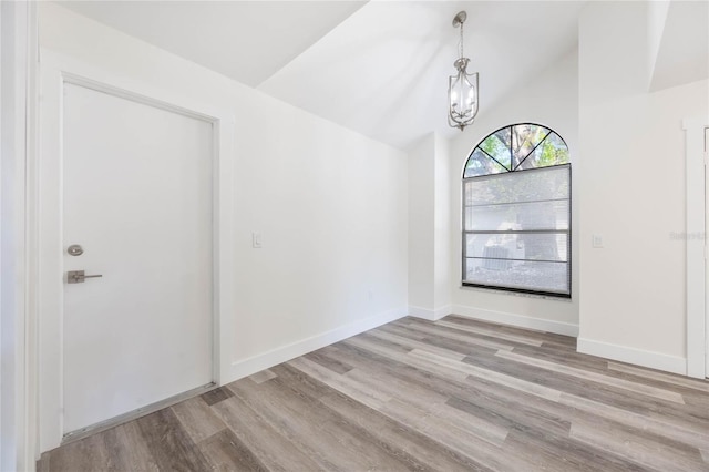 spare room with light hardwood / wood-style flooring, a notable chandelier, and vaulted ceiling