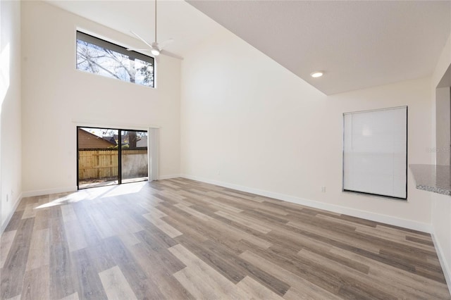 unfurnished living room with a towering ceiling, light hardwood / wood-style flooring, and ceiling fan