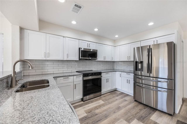 kitchen featuring sink, white cabinetry, stainless steel appliances, light stone counters, and light wood-type flooring