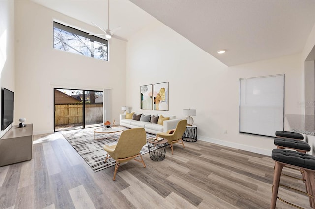 living room featuring ceiling fan, a towering ceiling, and light wood-type flooring