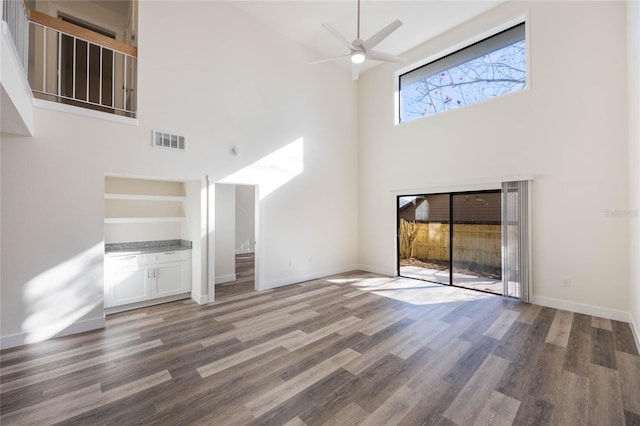 unfurnished living room featuring hardwood / wood-style floors, ceiling fan, and a high ceiling