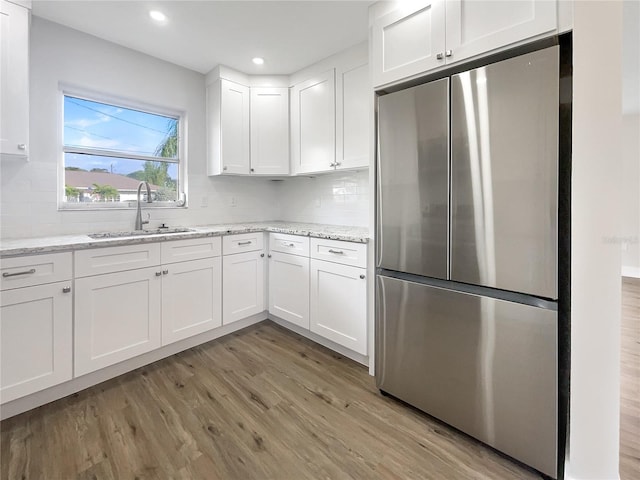 kitchen featuring sink, light stone counters, stainless steel fridge, light hardwood / wood-style floors, and white cabinets