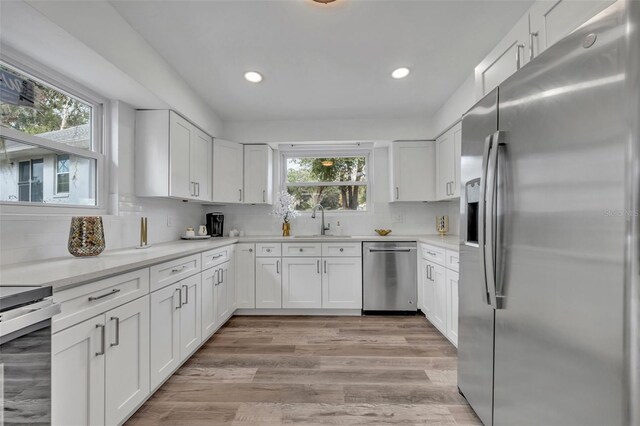 kitchen featuring sink, light hardwood / wood-style flooring, appliances with stainless steel finishes, white cabinets, and decorative backsplash
