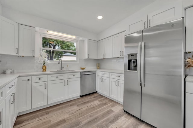 kitchen with stainless steel appliances, sink, white cabinets, and light hardwood / wood-style flooring