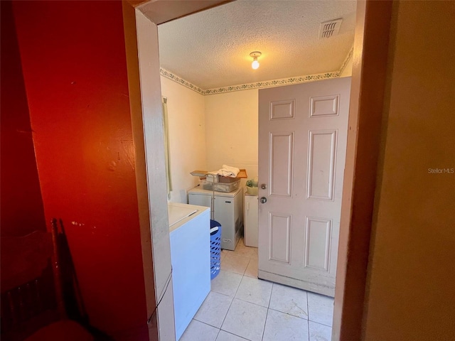 clothes washing area with washing machine and dryer, light tile patterned floors, and a textured ceiling