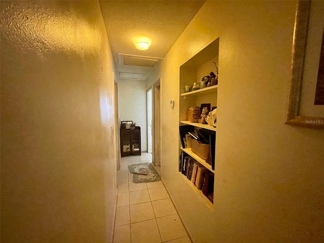 corridor with built in shelves, light tile patterned floors, and a textured ceiling