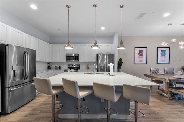 kitchen with white cabinetry, sink, hanging light fixtures, stainless steel appliances, and a center island with sink