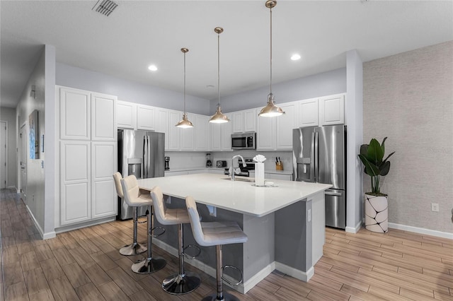 kitchen with a kitchen bar, appliances with stainless steel finishes, a center island with sink, decorative light fixtures, and white cabinets