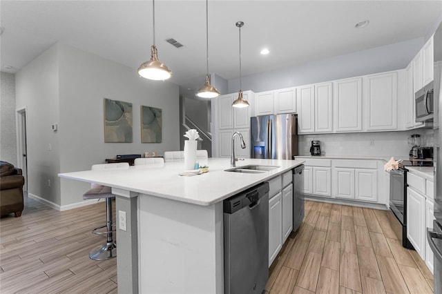 kitchen with white cabinetry, sink, hanging light fixtures, a center island with sink, and appliances with stainless steel finishes