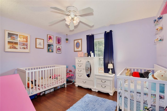 bedroom with a textured ceiling, ceiling fan, dark wood-type flooring, and a nursery area