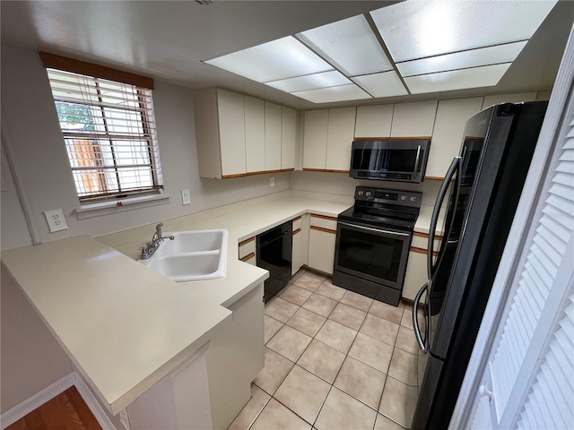 kitchen with light tile patterned flooring, a peninsula, a sink, light countertops, and black appliances