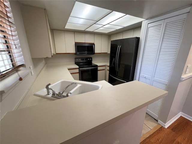 kitchen featuring light countertops, a sink, black appliances, a peninsula, and baseboards