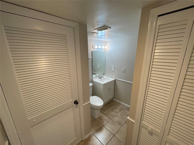 bathroom with a textured ceiling, tile patterned flooring, toilet, vanity, and a closet