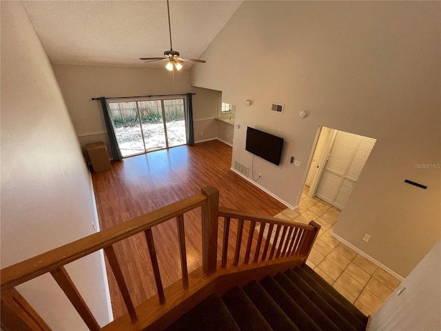 stairs featuring visible vents, a ceiling fan, high vaulted ceiling, baseboards, and tile patterned floors