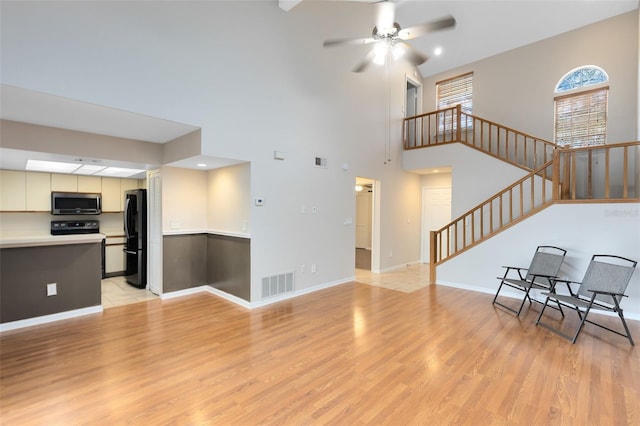 living room featuring light wood-style floors, visible vents, ceiling fan, and stairs