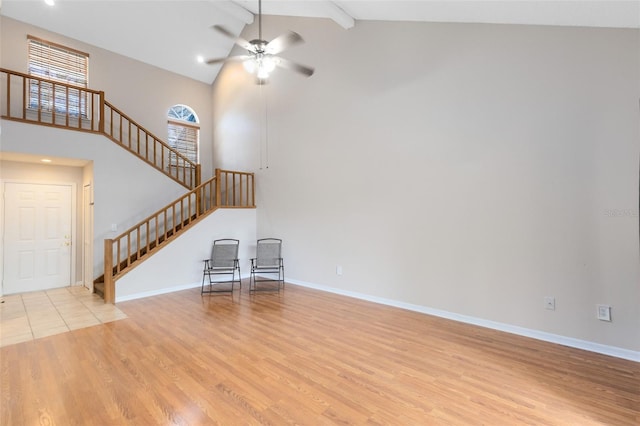 unfurnished living room featuring light wood-style floors, a ceiling fan, high vaulted ceiling, baseboards, and stairs