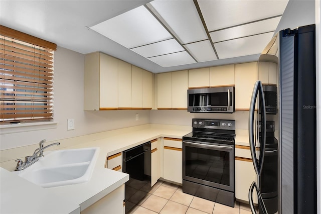 kitchen featuring cream cabinets, light countertops, a sink, and black appliances