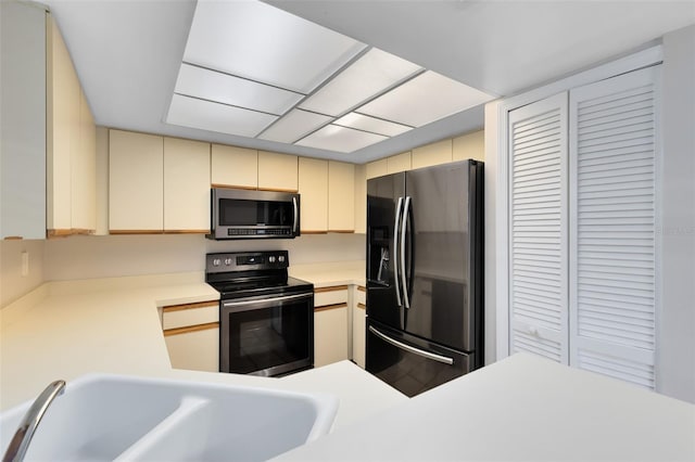 kitchen featuring appliances with stainless steel finishes, cream cabinetry, light countertops, and a sink