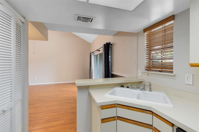 kitchen featuring a sink, visible vents, white cabinetry, vaulted ceiling, and light countertops