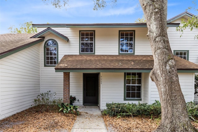 traditional-style home featuring roof with shingles and brick siding