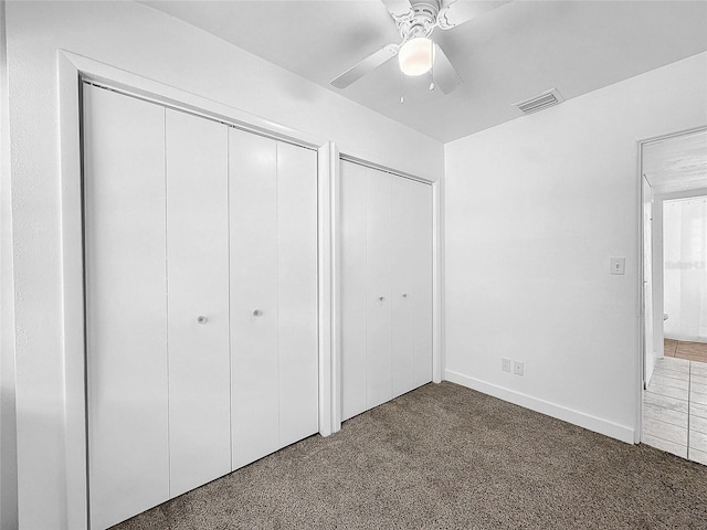 unfurnished bedroom featuring multiple closets, ceiling fan, and dark carpet