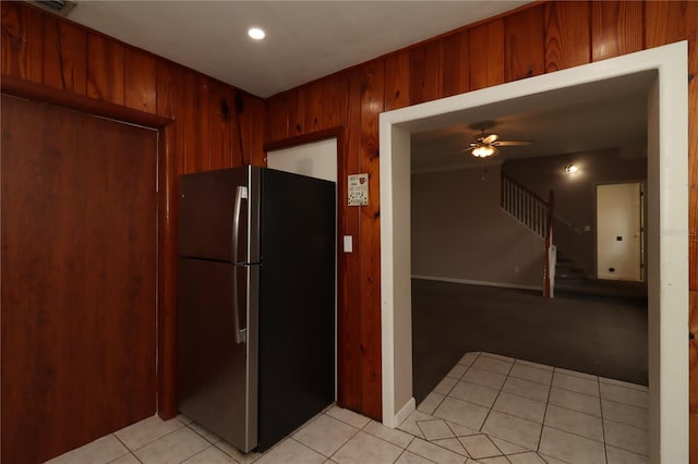 kitchen featuring ceiling fan, stainless steel fridge, light tile patterned floors, and wood walls