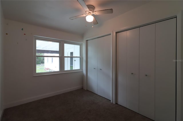 unfurnished bedroom featuring ceiling fan, dark carpet, and two closets