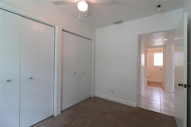 unfurnished bedroom with two closets, light carpet, and ceiling fan