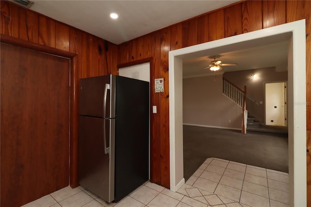 kitchen with light tile patterned flooring, ceiling fan, stainless steel fridge, and wooden walls