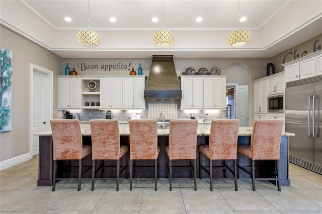 kitchen featuring built in appliances, decorative light fixtures, a spacious island, and custom range hood