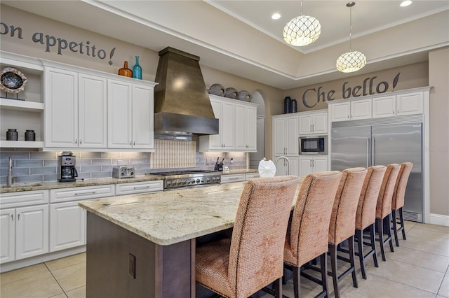 kitchen featuring built in appliances, premium range hood, white cabinetry, and a kitchen island with sink